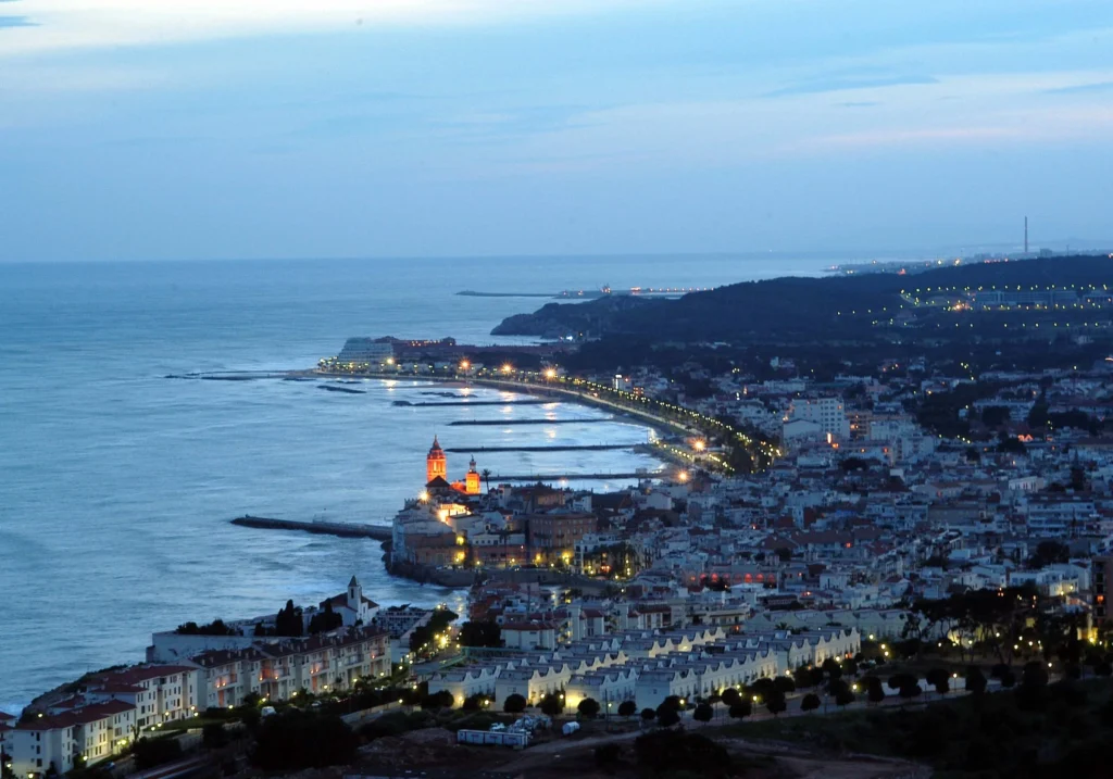 Night view of illuminated Sitges from a hilltop, with the sea in the background