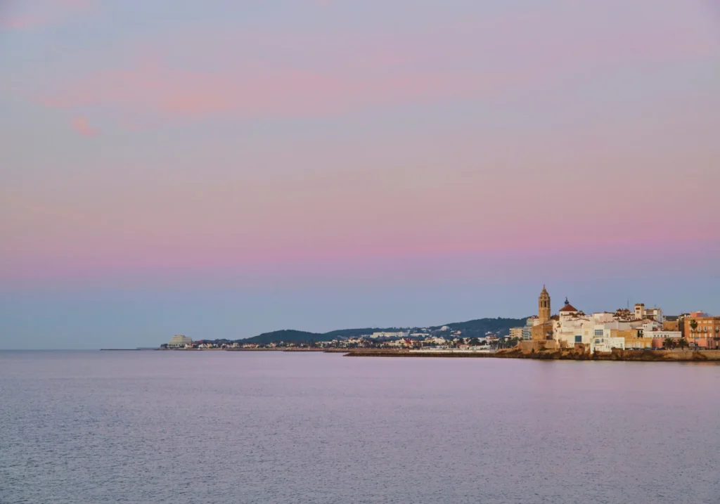 Silhouette of Sitges church and old town reflected on the calm sea at dawn