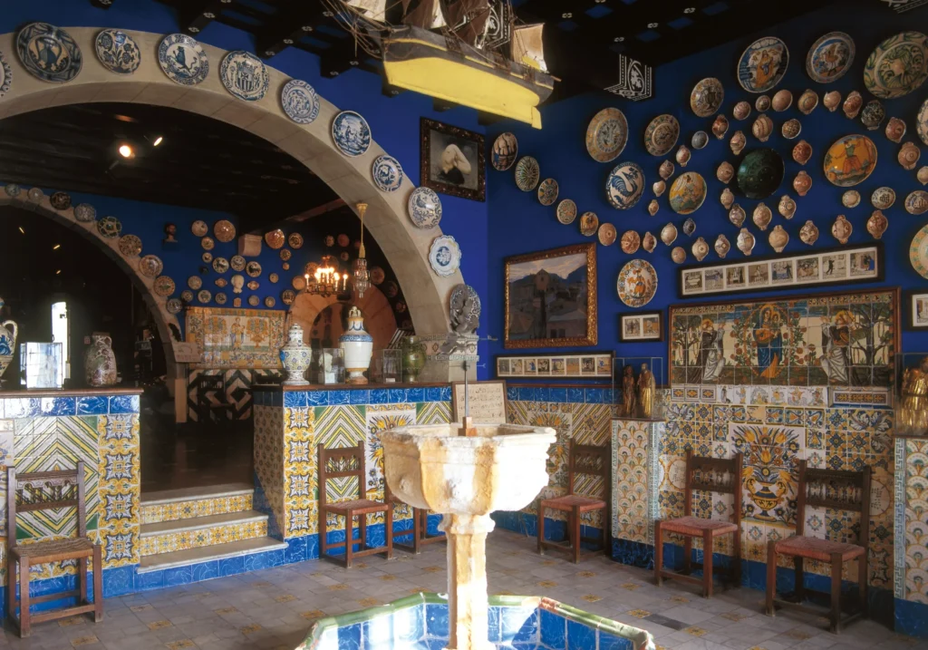 Room at Cau Ferrat Museum with blue walls decorated with ceramic plates and a stone fountain
