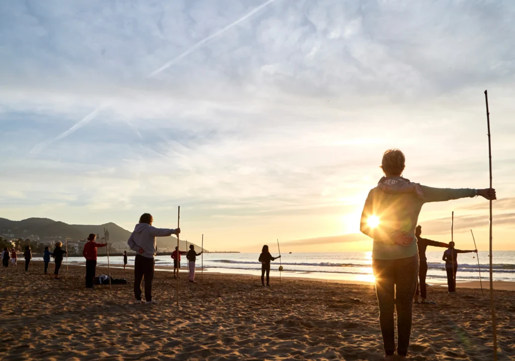 People exercising with sticks on Sitges beach at sunset