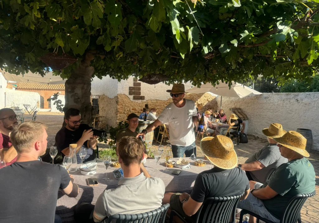 Group enjoying a wine tasting under a tree in the outdoor area of a winery