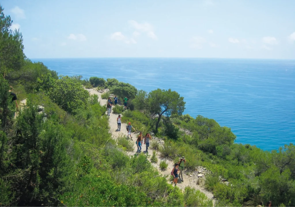 Hikers walking along a coastal path with views of the blue Mediterranean Sea in Sitges