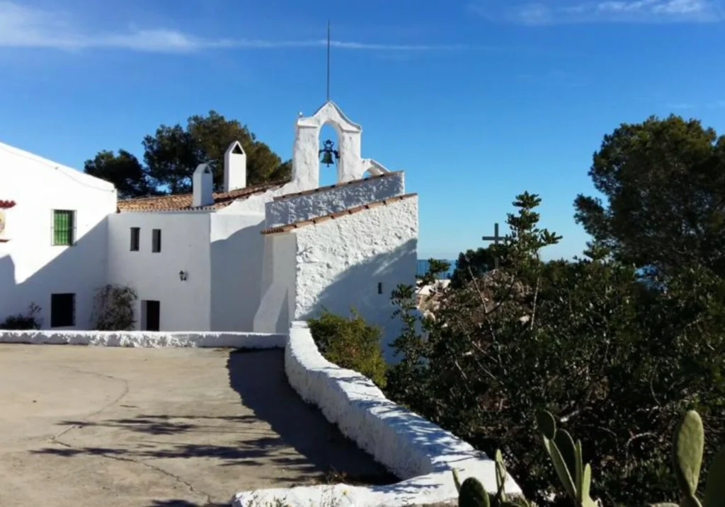 White hermitage with bell tower surrounded by Mediterranean vegetation and cacti in Sitges