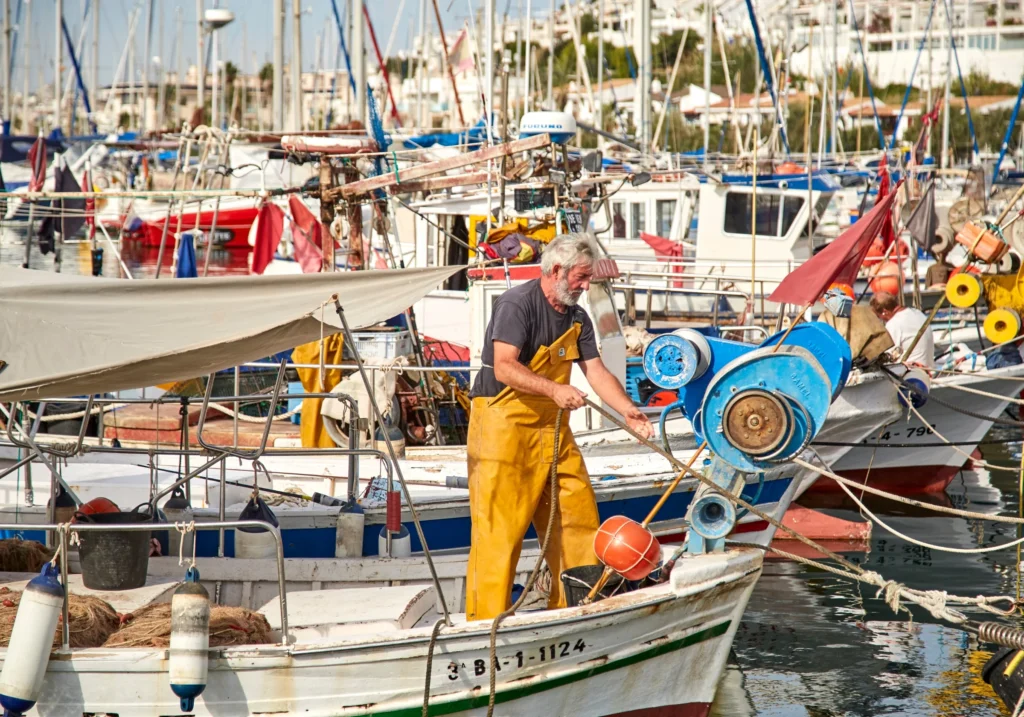 Fisherman working on his boat in Sitges harbour with other vessels in the background