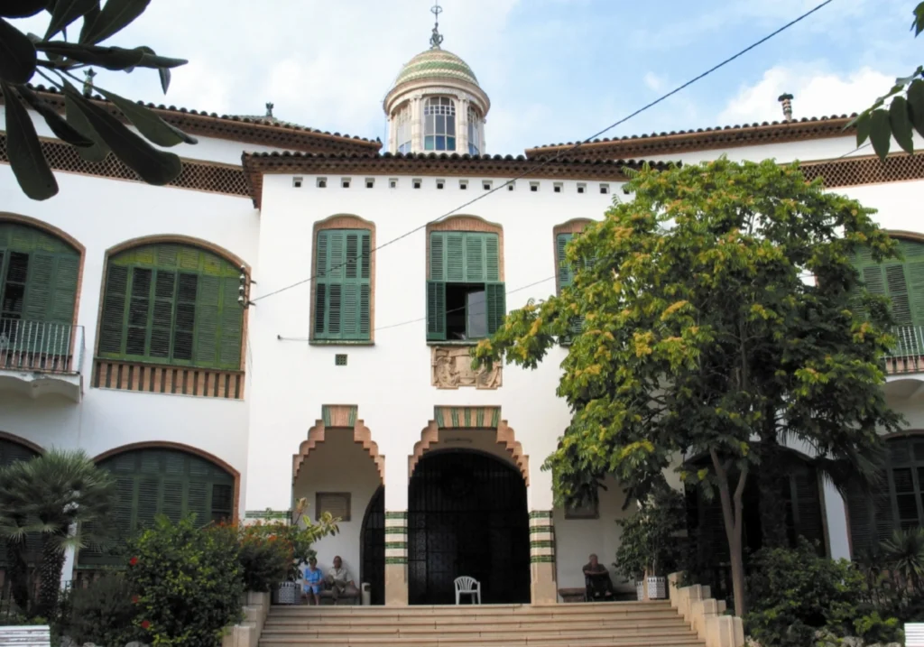 White Modernista building with a dome and green shuttered windows in Sitges