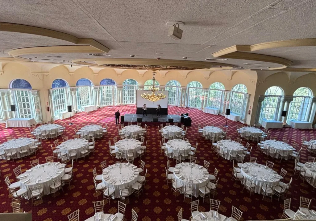 Gala hall with round tables set for a gala dinner, arched windows and a crystal chandelier