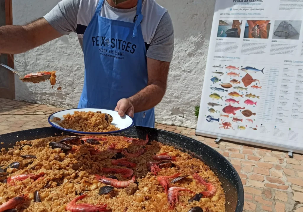 Peix Sitges cook serving a seafood paella from a large pan