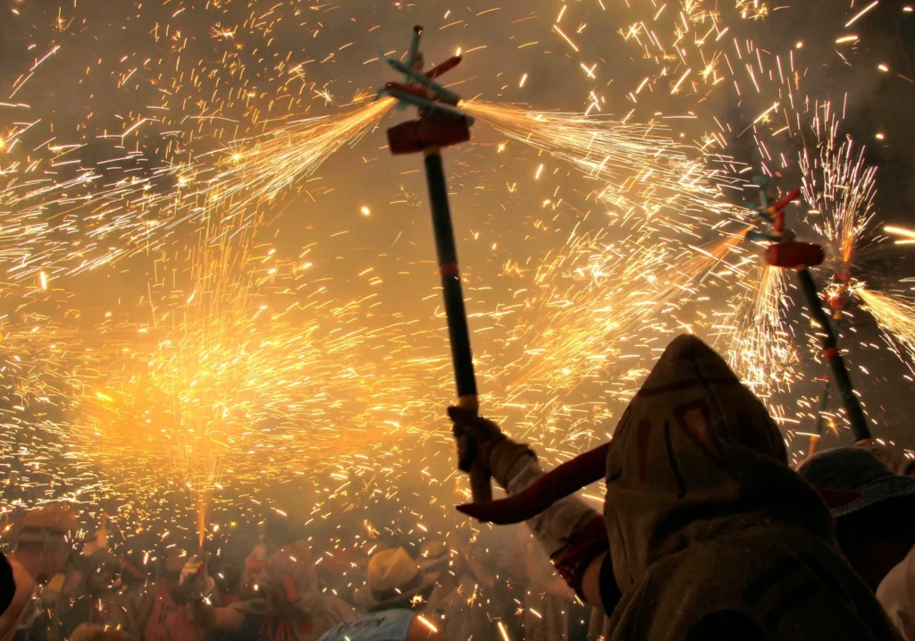 Night-time correfoc fire run with sparks and devil figures during Sitges festivities