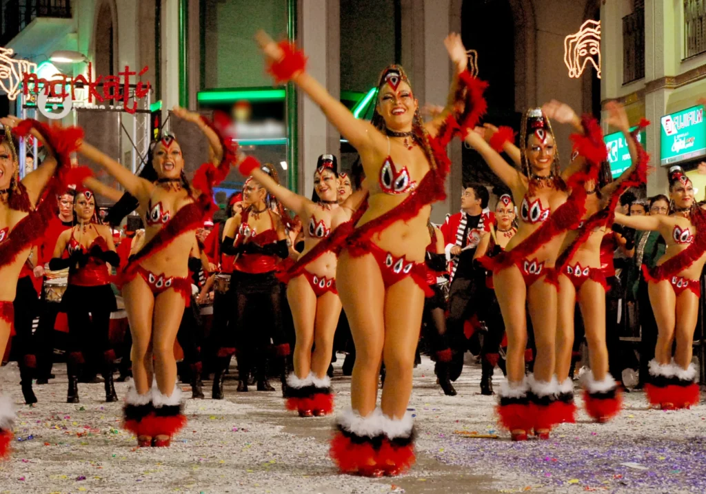 Dancers in vibrant red costumes performing during the Sitges Carnival night parade